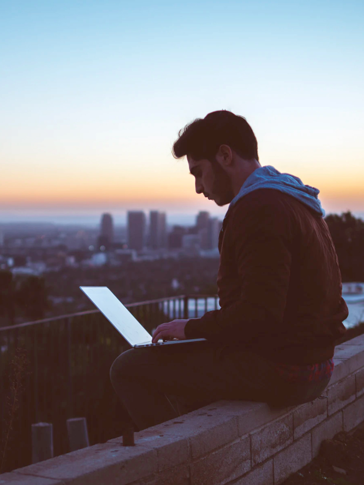 Man overlooking city at sunset on laptop