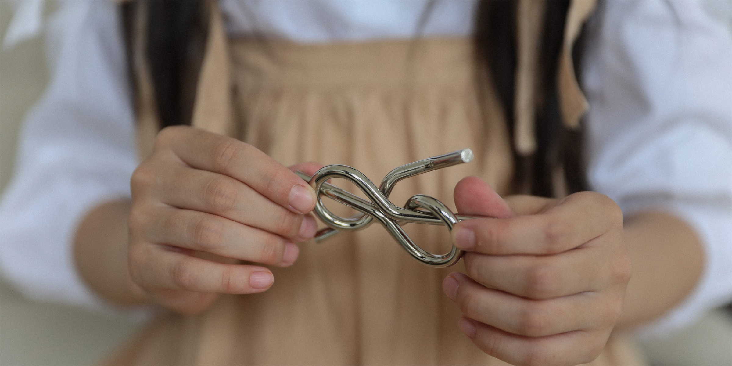 Close up image of two hands holding a twisted metal tangle puzzle
