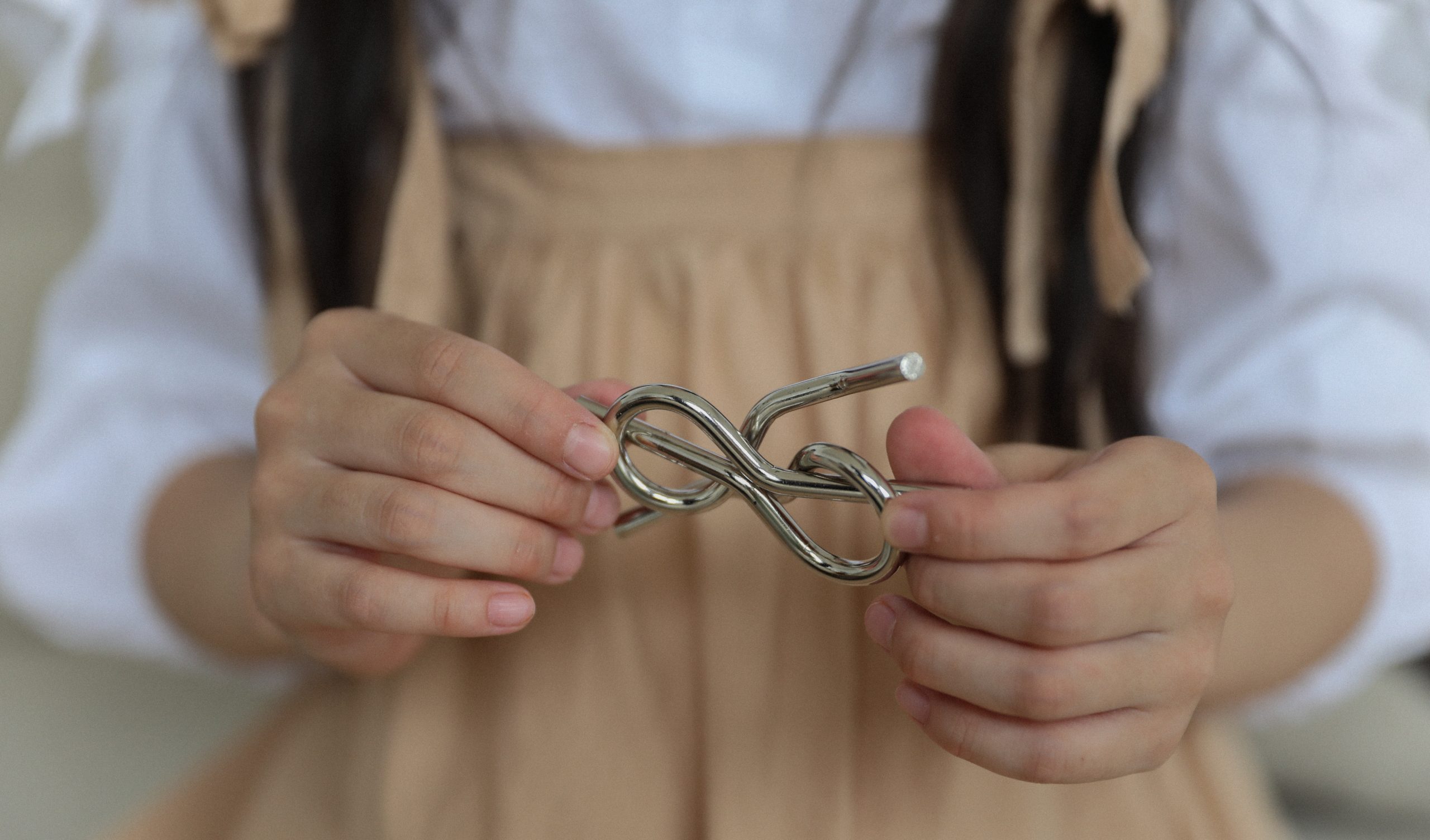 close up image of two hands holding a twisted metal tangle puzzle
