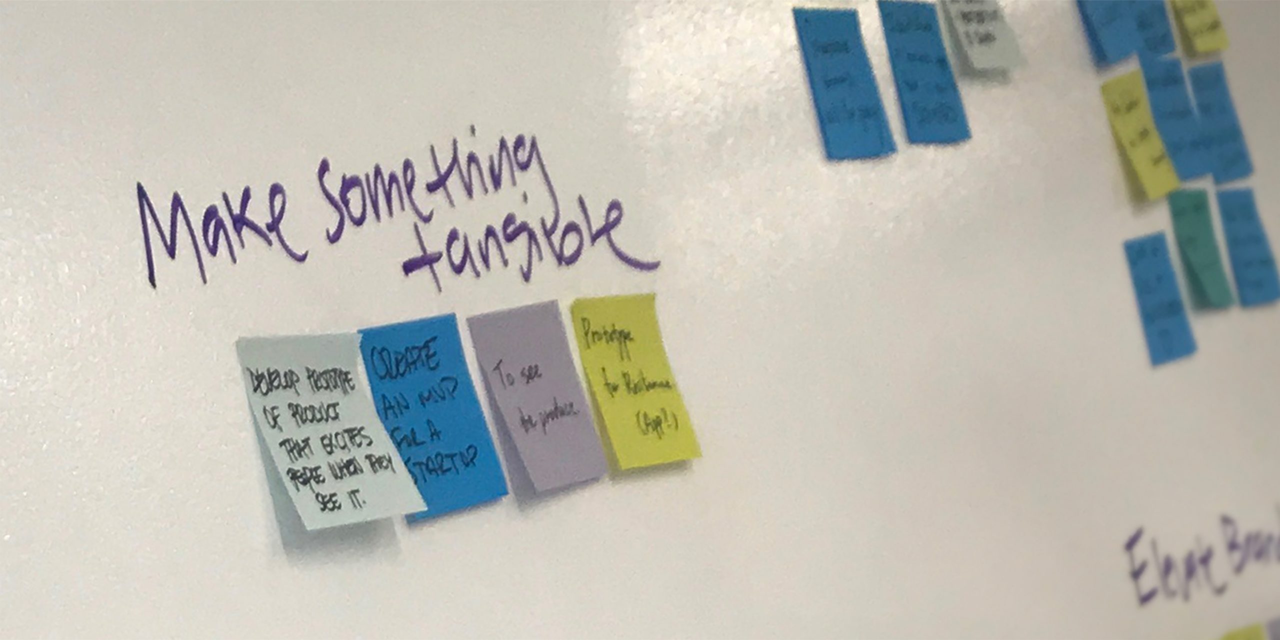 Photo of a whiteboard with the words "make something tangible" written on it and sticky notes beneath