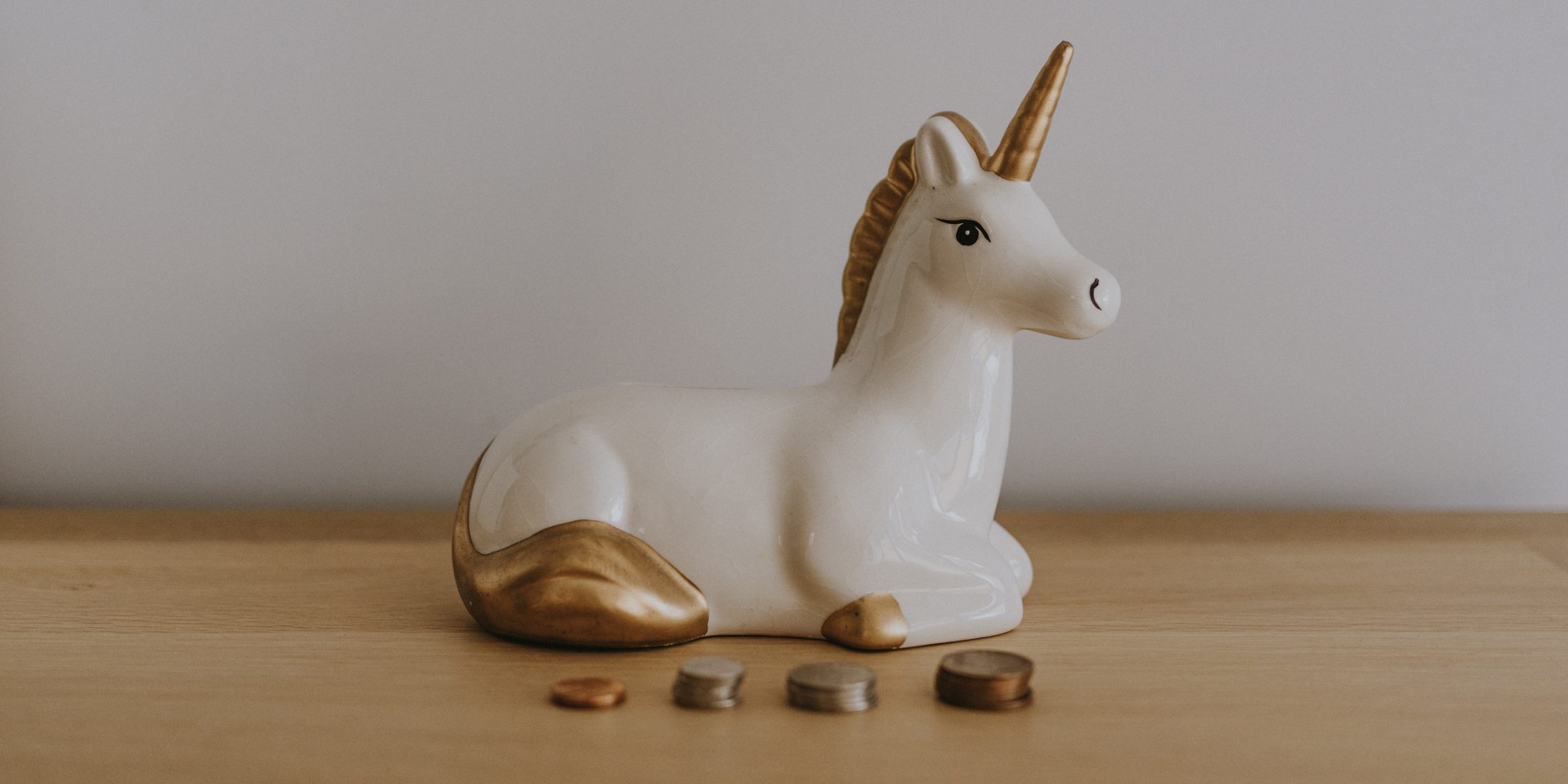 unicorn "piggy" bank on a desk with several stacks of coints