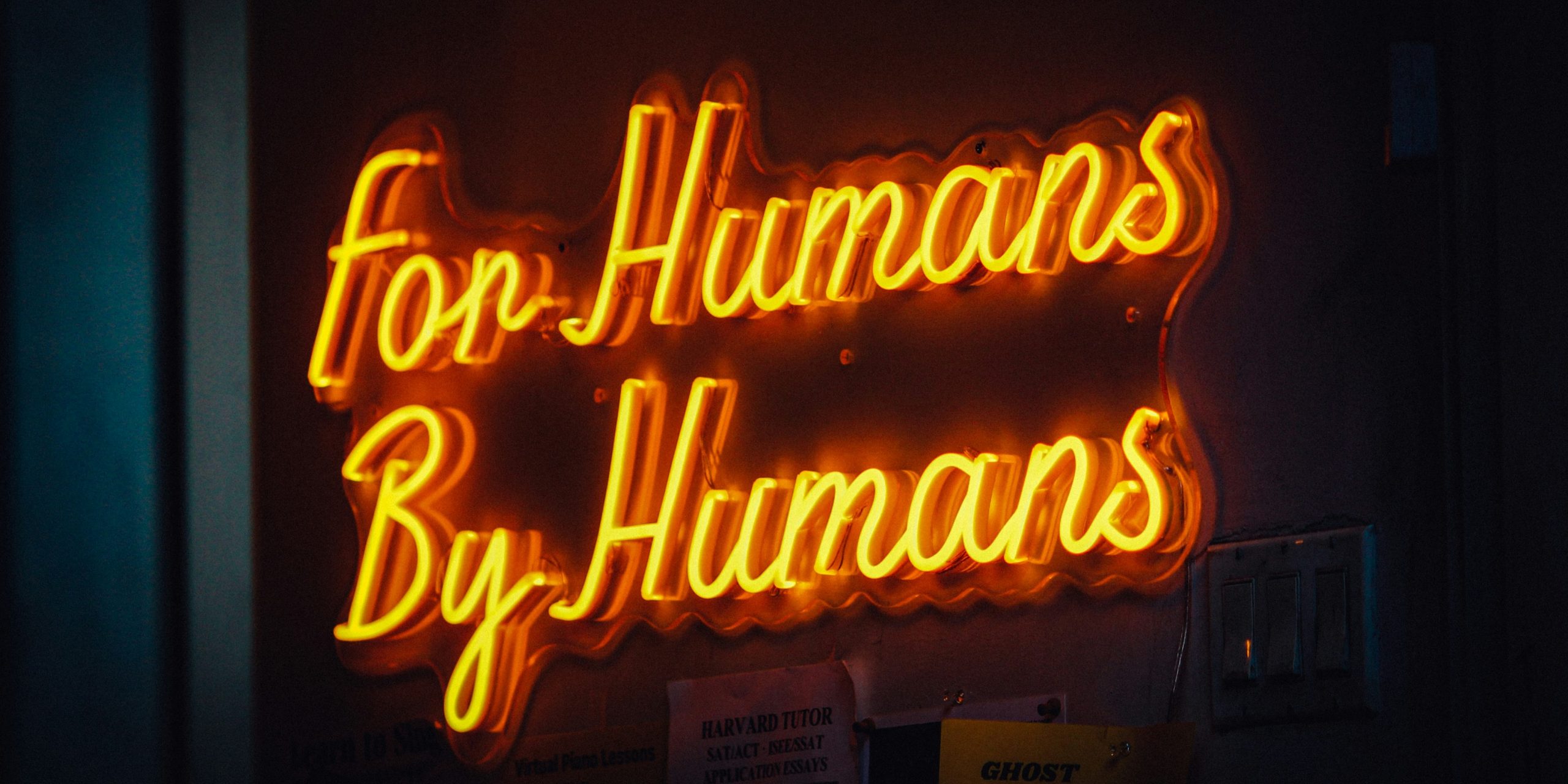 Florescent sign that reads for humans by humns in a handwritten script