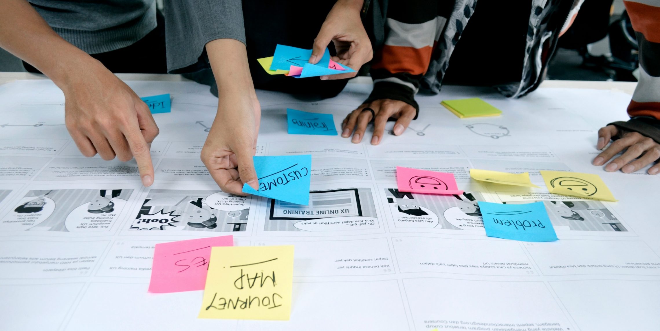 Insurance doesn't need to be explained. This image shows the hands of designers using sticky notes on a table with interfaces to design a better insurance experience.